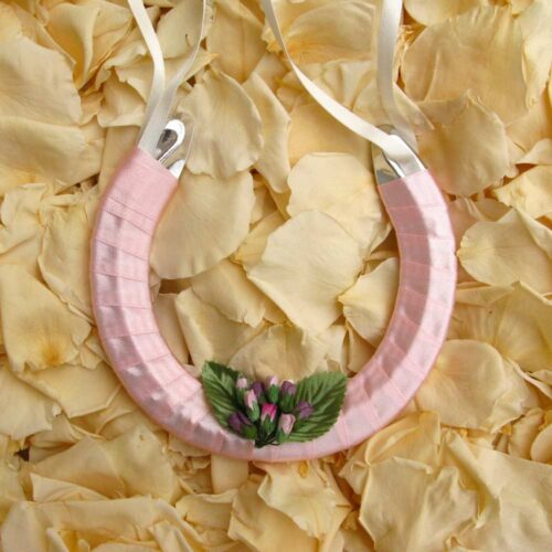 A lucky wedding horseshoe for the bride decorated with lilac rose buds, green leaves and pale pink ribbon.